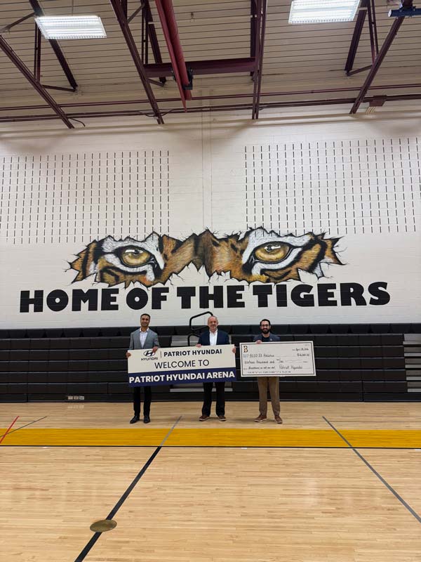 Three people standing in a gym holding a welcome sign