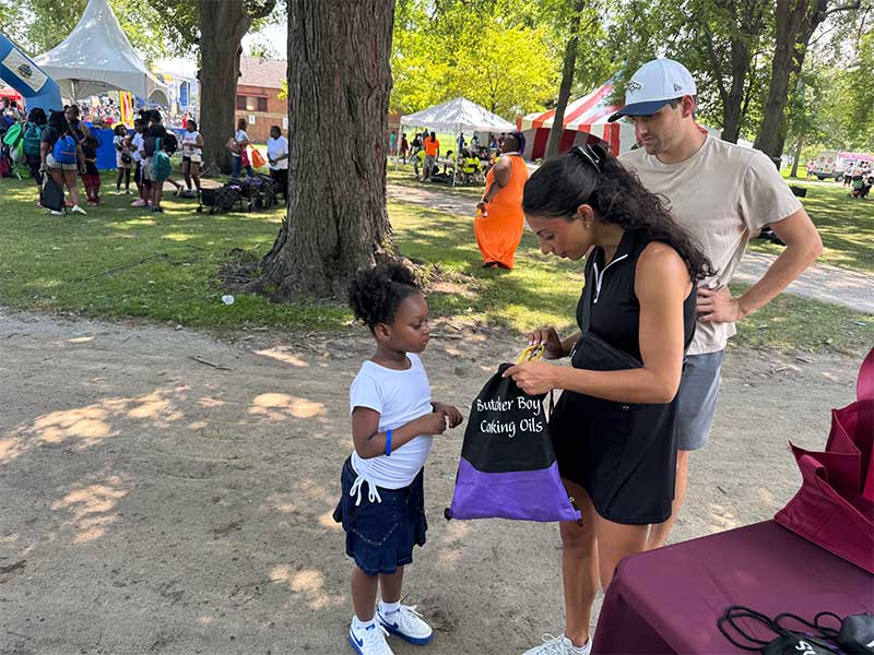 Person handing a giveaway bag to a child at an outdoor community event.