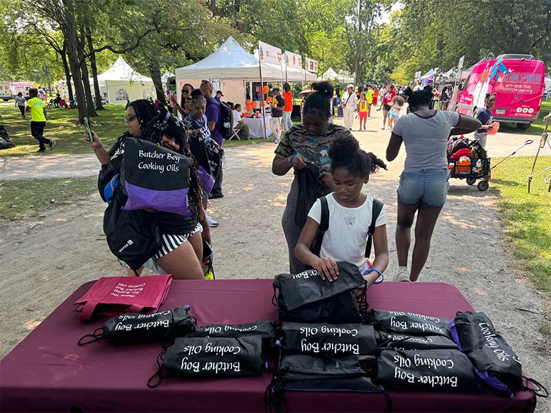 Person selecting a giveaway bag from a table at an outdoor community event.